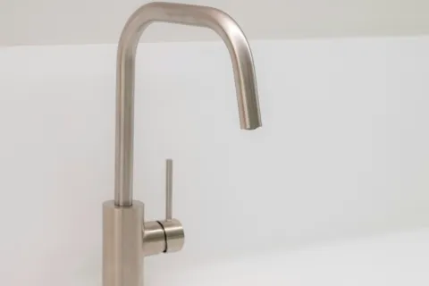 Modern stainless steel kitchen faucet over a clean white sink with minimalist design.
