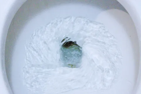 Water swirling and draining rapidly in a white toilet bowl during flushing in a bright setting
