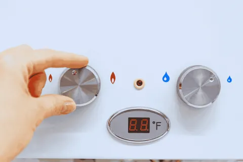 Hand adjusting the temperature knob on a white water heater control panel with digital display showing Fahrenheit.