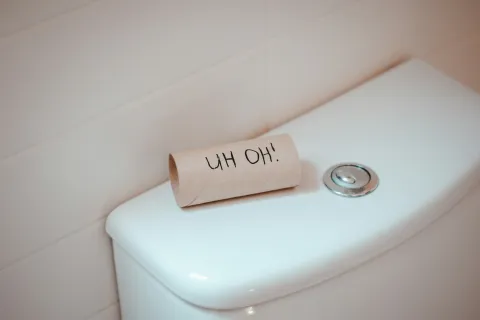 Empty toilet paper roll with UH OH text placed on a white toilet tank lid in a bathroom.