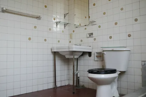 Small bathroom with white tiles decorated with yellow flower patterns, a white sink, and a toilet with a black seat.