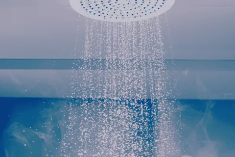 Steam rising from hot water pouring from a round ceiling showerhead against a blue background