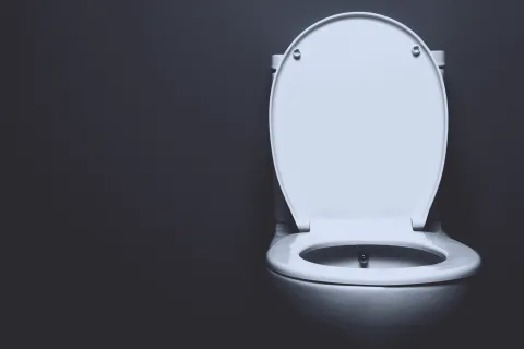 White toilet with open lid against a dark gray background in a minimalist bathroom setting