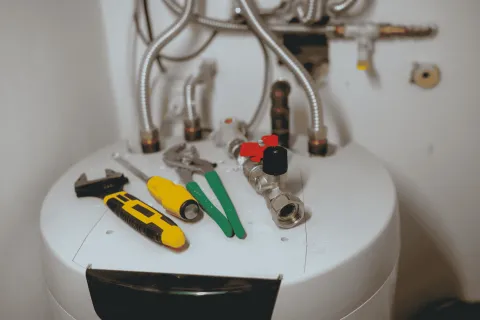 Plumbing tools including wrench, screwdriver, pliers, and valves on top of a white water heater tank.