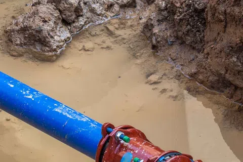 Blue and black water pipes connected by a red coupling in muddy trench with wet soil surrounding.