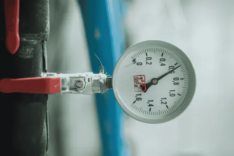 Close-up of a pressure gauge attached to a black pipe with a red valve handle in a mechanical setting.