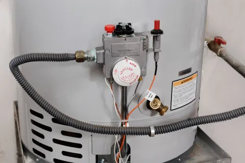 Close-up of a water heater with plumbing and safety features clearly visible.