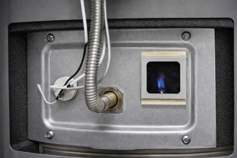 Close-up of a gas furnace burner igniting with blue flame inside metal housing and connected wires.