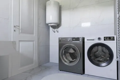 Modern laundry room with white tiled walls, paired front-load washer and dryer, and a white water heater.