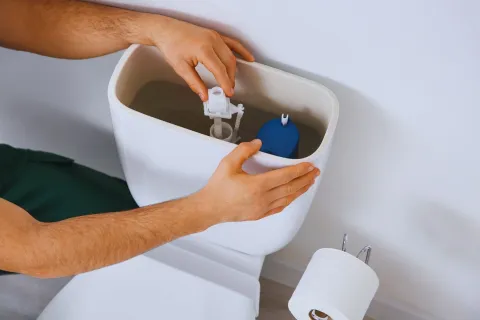 Person repairing or adjusting the inner mechanisms of a toilet tank with visible water and components.