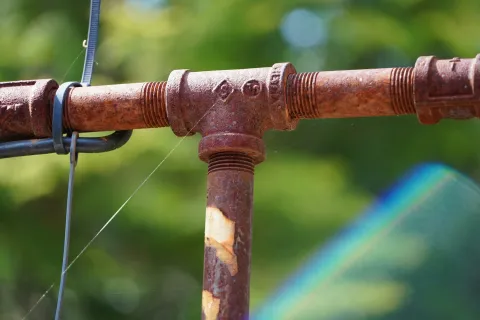 Close-up of a rusted metal pipe joint with zip tie and green blurred background.