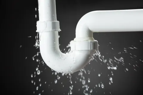 Close-up of a white plumbing pipe joint leaking water against a dark background.