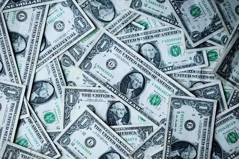 Pile of scattered one dollar bills showing George Washington's portrait and green treasury seals.