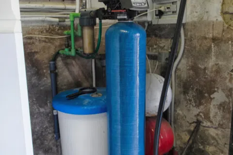 Blue water softener tank and brine tank in a basement with pipes and control valve setup.