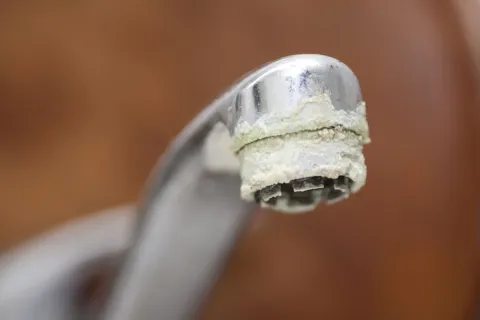 Close-up of a metal faucet with white mineral deposits and limescale buildup around the spout tip.