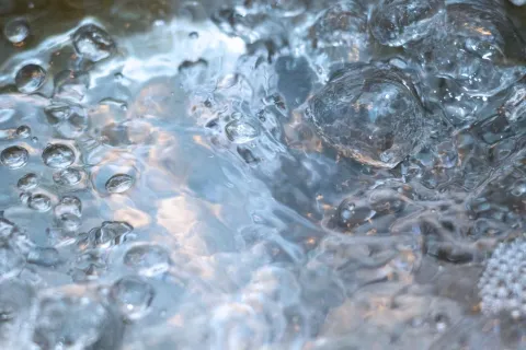 Close-up of bubbling, boiling water with rising steam and water droplets in motion.