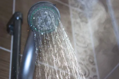 Close-up of water streaming from a silver showerhead with steam rising in a tiled bathroom.