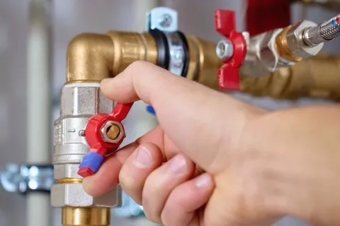 Close-up of hand turning a red valve on a brass plumbing pipe with metal fittings and connectors