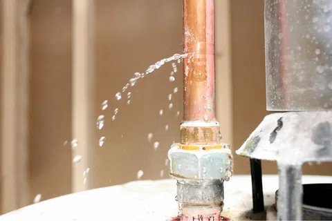Copper pipe leaking water through a small hole near a joint inside a building.