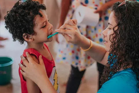 Woman helping young boy brush his teeth during a dental care activity indoors.