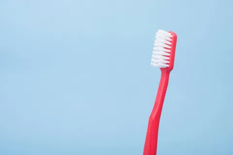Red toothbrush with white bristles on a light blue background for dental hygiene.