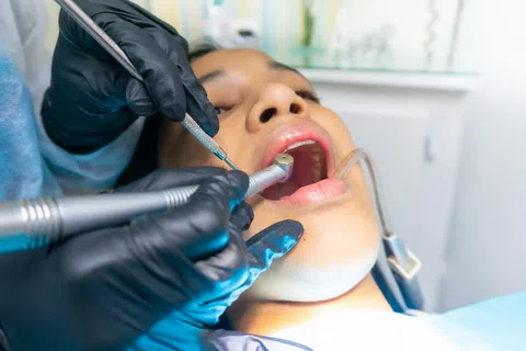 Close-up of dental treatment showing dentist with gloves working inside patient's open mouth using dental instruments.