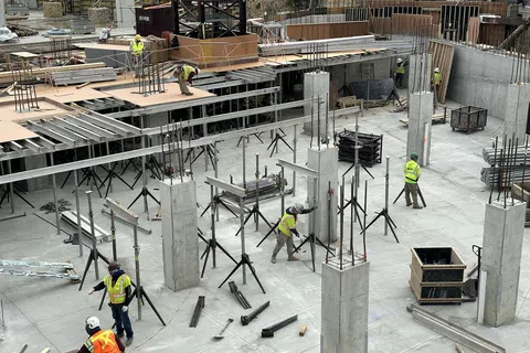 Construction workers in safety vests on concrete building site with steel supports and pillars under assembly