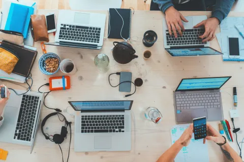 Overhead view of a collaborative workspace with laptops, notebooks, coffee, and people working together.