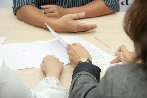 Two people discussing documents during a meeting at a wooden table, focusing on hands and paperwork.