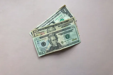 Twenty and one dollar US bills on a plain light pink background with clear details and currency markings.