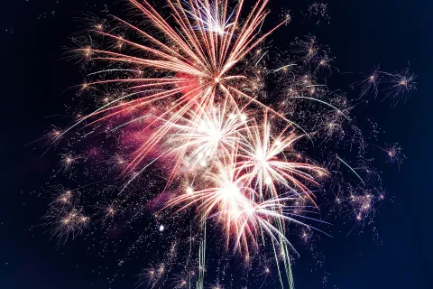 Bright white and red fireworks exploding against a dark night sky during a celebration event.