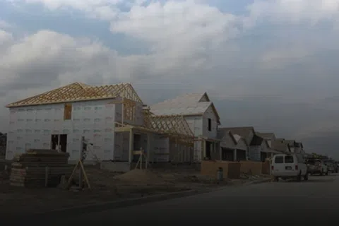 Row of houses under construction with wooden framing and building materials on a cloudy day.