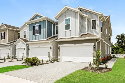 Row of modern suburban two-story townhouses with garages and neatly landscaped yards under clear blue sky.