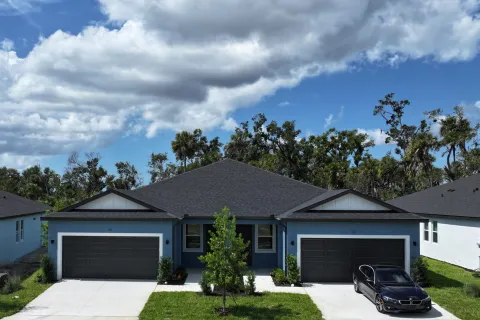 Modern duplex house with dark roofs, two-car garages, a black car parked, and a partly cloudy blue sky.