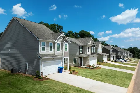 Modern suburban houses with garages and lawns under a blue sky with scattered clouds on a sunny day