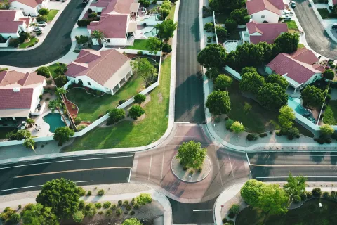 Aerial view of a suburban neighborhood with red-roof houses, green lawns, and a roundabout intersection.
