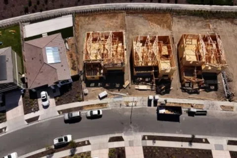 Aerial view of three wooden houses under construction next to completed homes in a residential neighborhood.