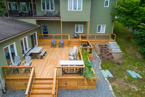 Spacious wooden backyard deck with outdoor chairs, tables, railings, and stairs leading to gravel path and garden area.