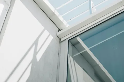 Modern building corner with glass window, white railings, smooth concrete wall, and clear blue sky.