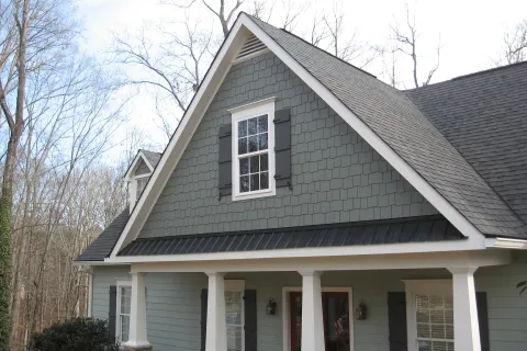 Charming house exterior with gray shingles, decorative trim, and large windows against a natural backdrop.