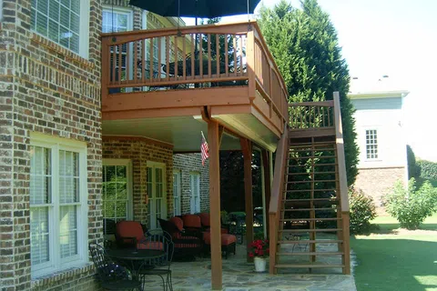 Raised wooden deck with stairs and outdoor seating area under covered patio beside brick house.