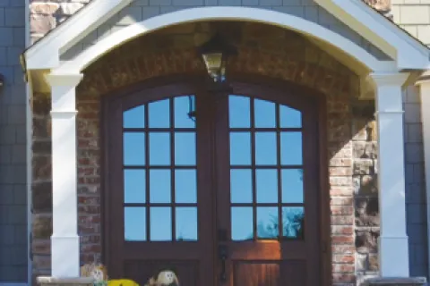 Charming front entrance featuring double wooden doors, stone facade, and seasonal decorations.