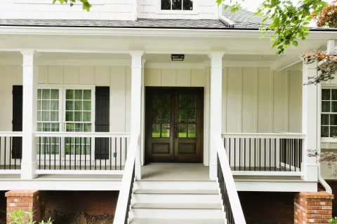 Front view of a white house porch with stairs, black railing, dark wooden double doors, and large windows.