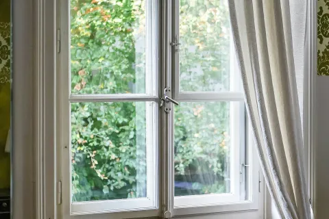 Bright white window with sheer curtain and wooden bench, green foliage visible outside through glass panes