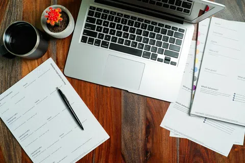 Laptop, documents, pen, coffee cup, and small cactus on wooden desk for workspace setup