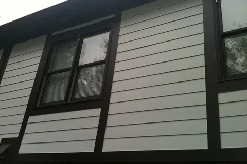 Exterior of a house with white horizontal siding and dark brown trim around windows and panels.