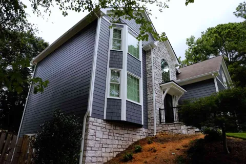 Modern two-story house with gray siding and stone exterior surrounded by trees and landscaping.