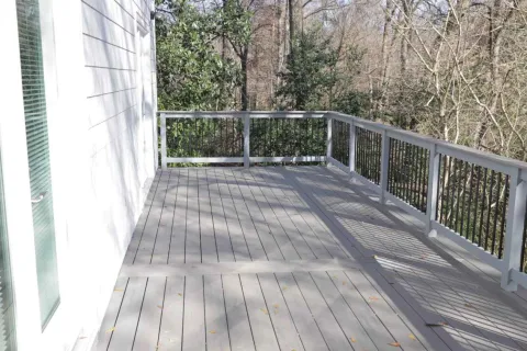 Spacious wooden deck attached to house with metal railing and trees in background on a sunny day