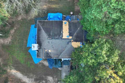 Aerial view of a house undergoing roof repair with workers and blue tarps surrounding the area