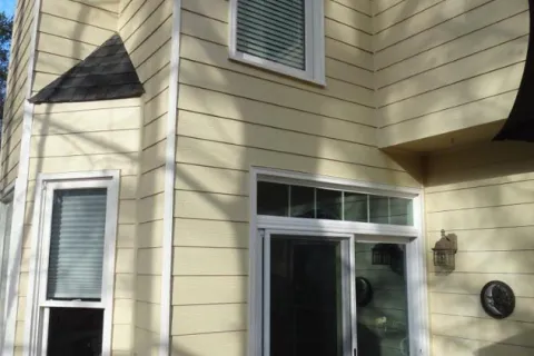 Yellow house exterior with white trim windows and sliding glass door on wooden deck with holiday wreath.